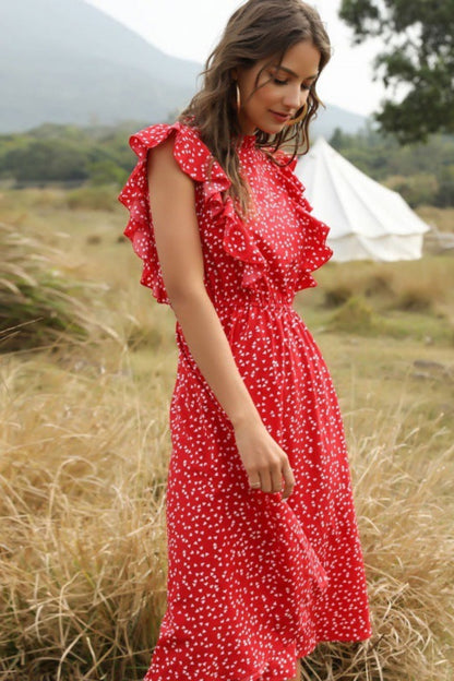 Woman in a red dress with white polka dots standing in a grassy field with a tent in the background.