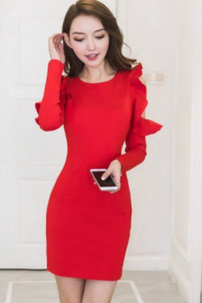 Woman wearing a red dress with ruffled sleeves in a minimal indoor setting.