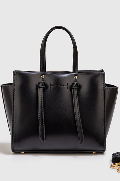 Black handbag with a matching strap on a light gray background