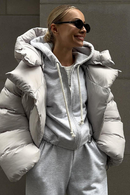 Person wearing a gray puffer jacket and matching outfit against a gray wall.