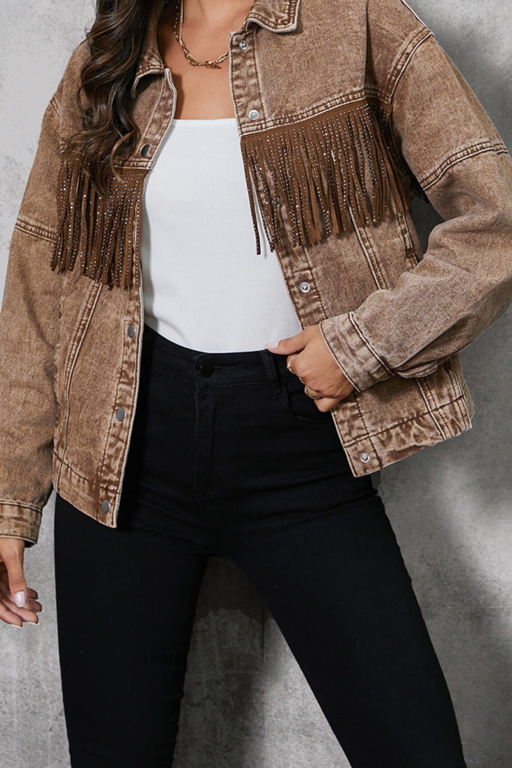Person wearing a brown fringed denim jacket over a white top and black pants on a gray background
