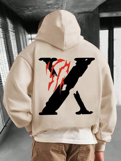 Person wearing a beige hoodie with a black and red logo on the back, standing indoors.