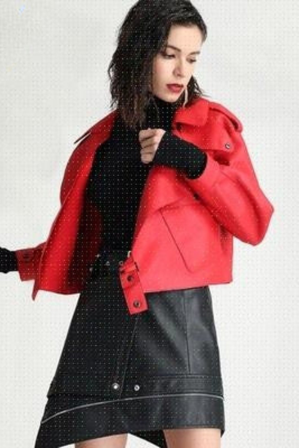 Woman wearing a red jacket over a black outfit with white polka dots on a light gray background