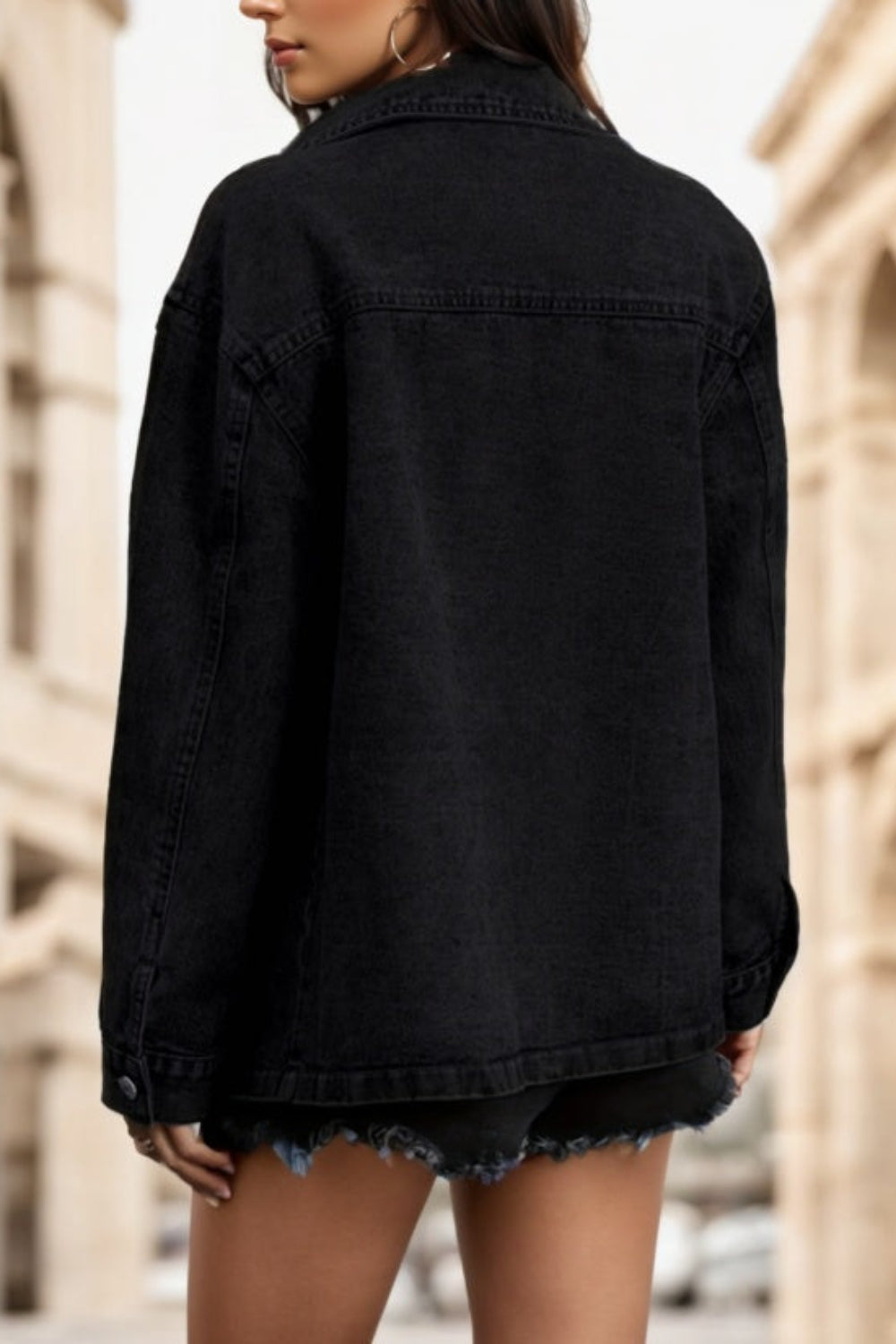 Person wearing a black denim jacket with a blurred architectural background