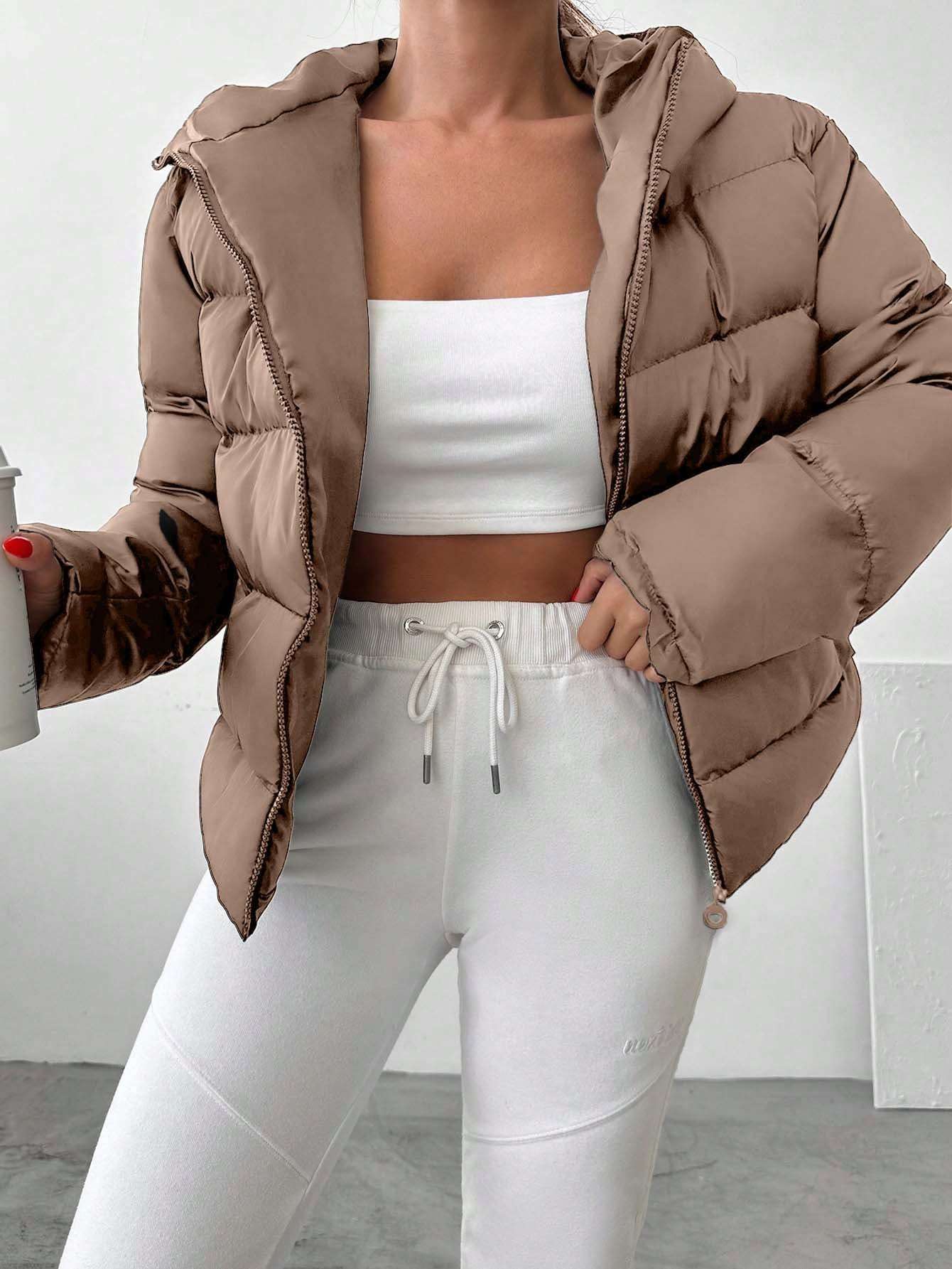 Person wearing a brown puffer jacket over a white top and pants on a plain background