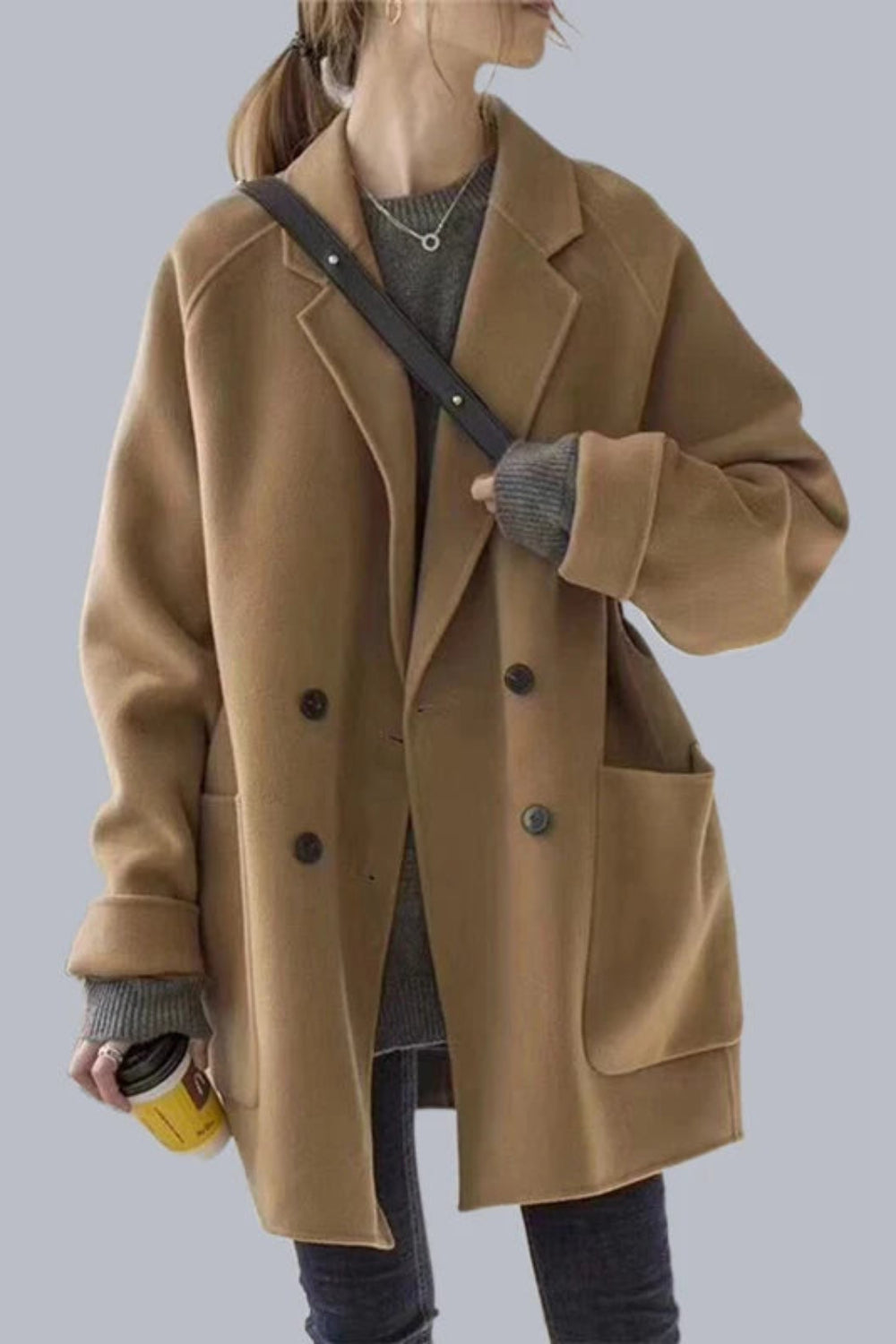 Person wearing a brown coat holding a yellow cup against a plain background