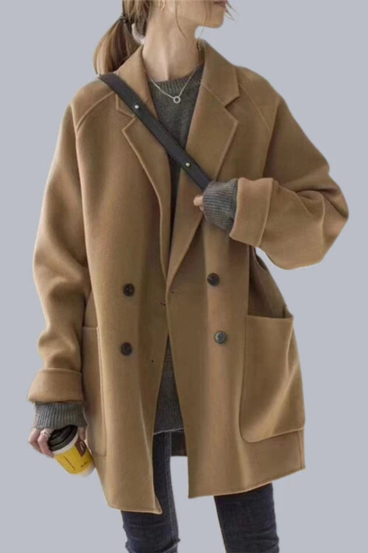 Person wearing a brown coat holding a yellow cup against a plain background