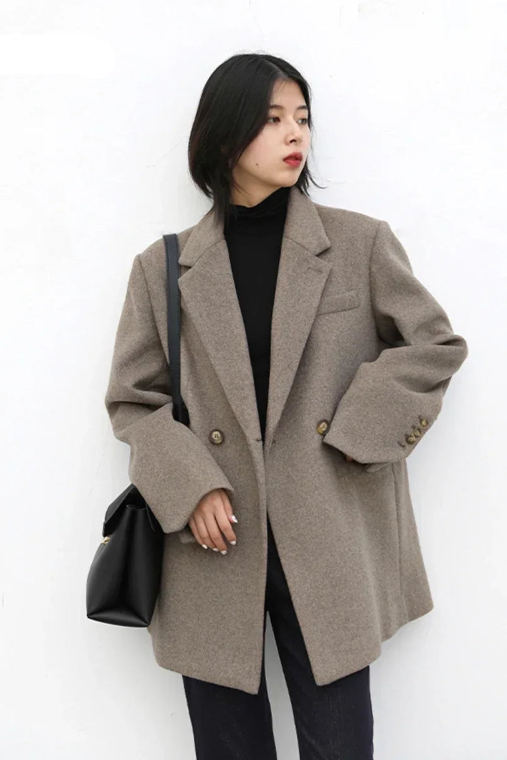 Woman wearing a beige coat holding a black bag against a white background