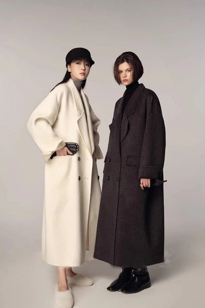 Two people wearing long coats on a plain background