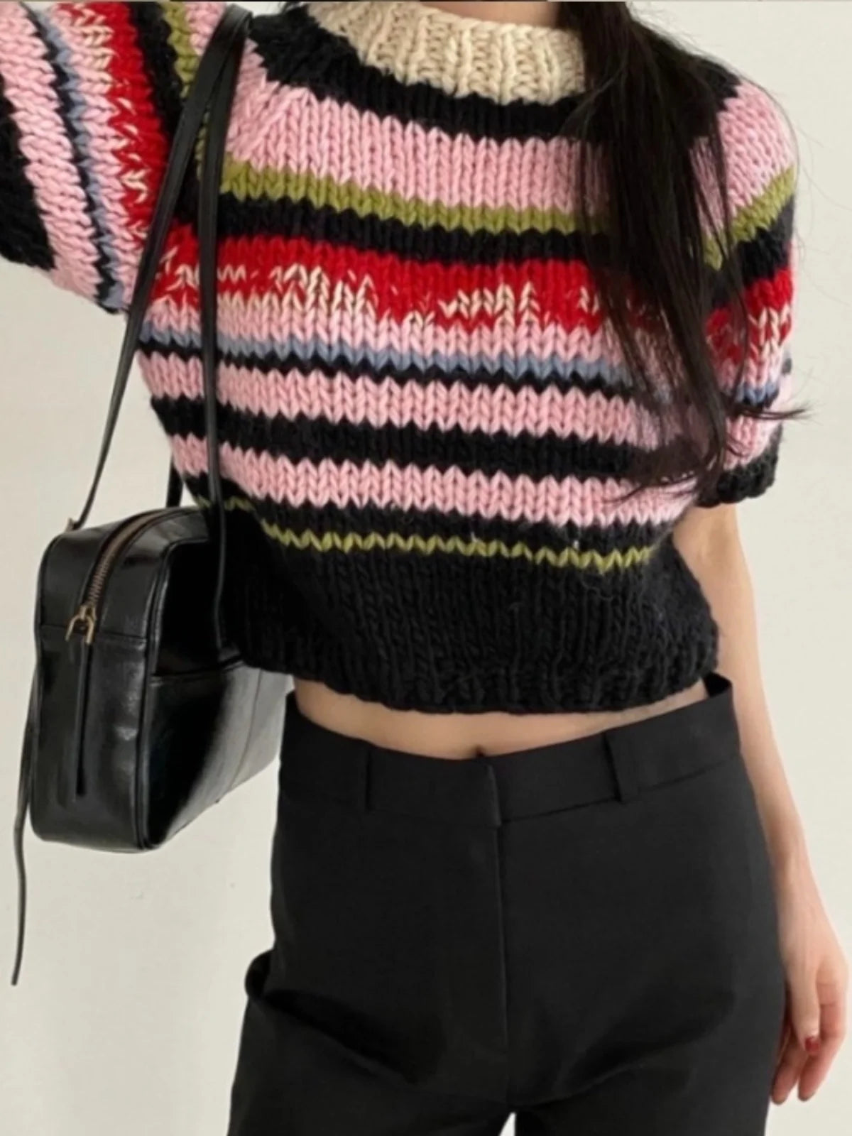 Person wearing a colorful striped sweater and black pants with a black bag.