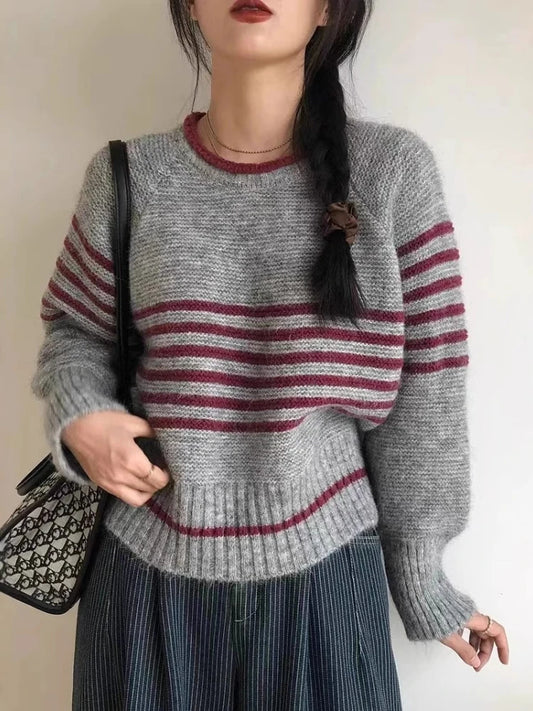 Person wearing a gray sweater with red horizontal stripes, holding a black handbag.