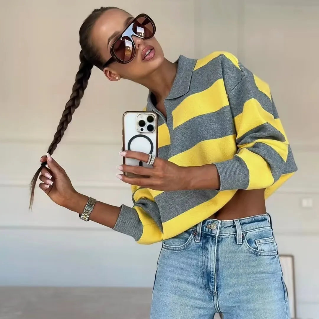 Person wearing a yellow and gray striped sweater and blue jeans, taking a selfie.