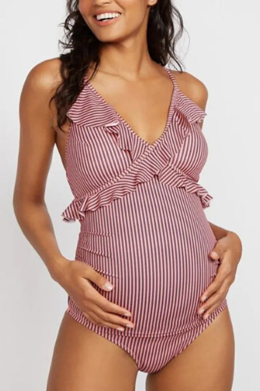 A pregnant woman wearing a red and white striped one-piece swimsuit with a v-neckline and ruffled detailing.