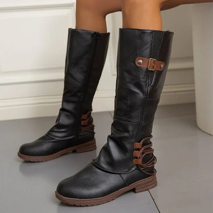 Black knee-high boots with brown accents on a neutral background