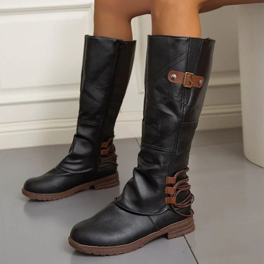 Black knee-high boots with brown accents on a neutral background