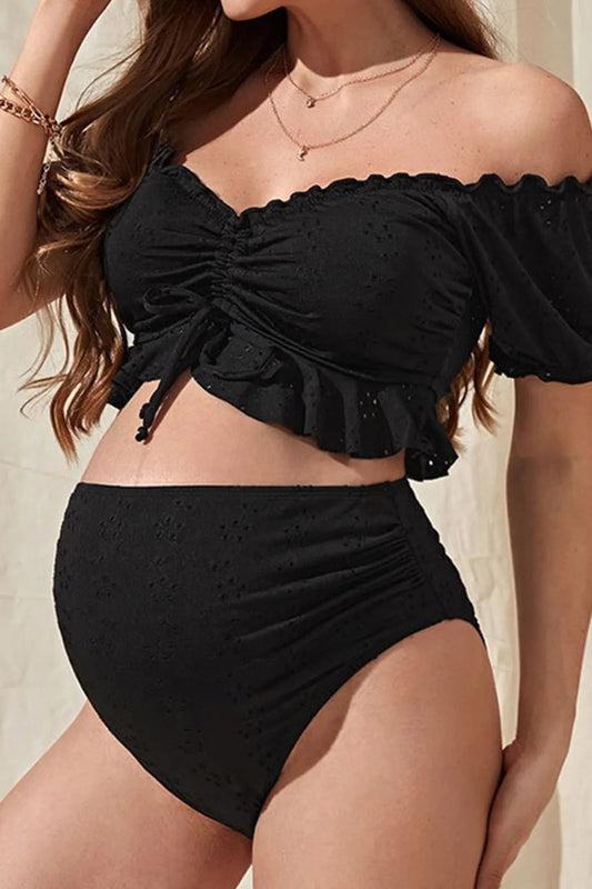 A pregnant woman wearing an off-shoulder black bikini set with tie-front design.