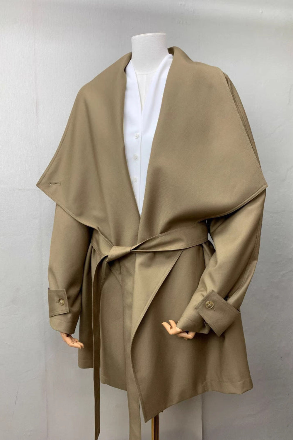 Beige trench coat on a mannequin against a plain background
