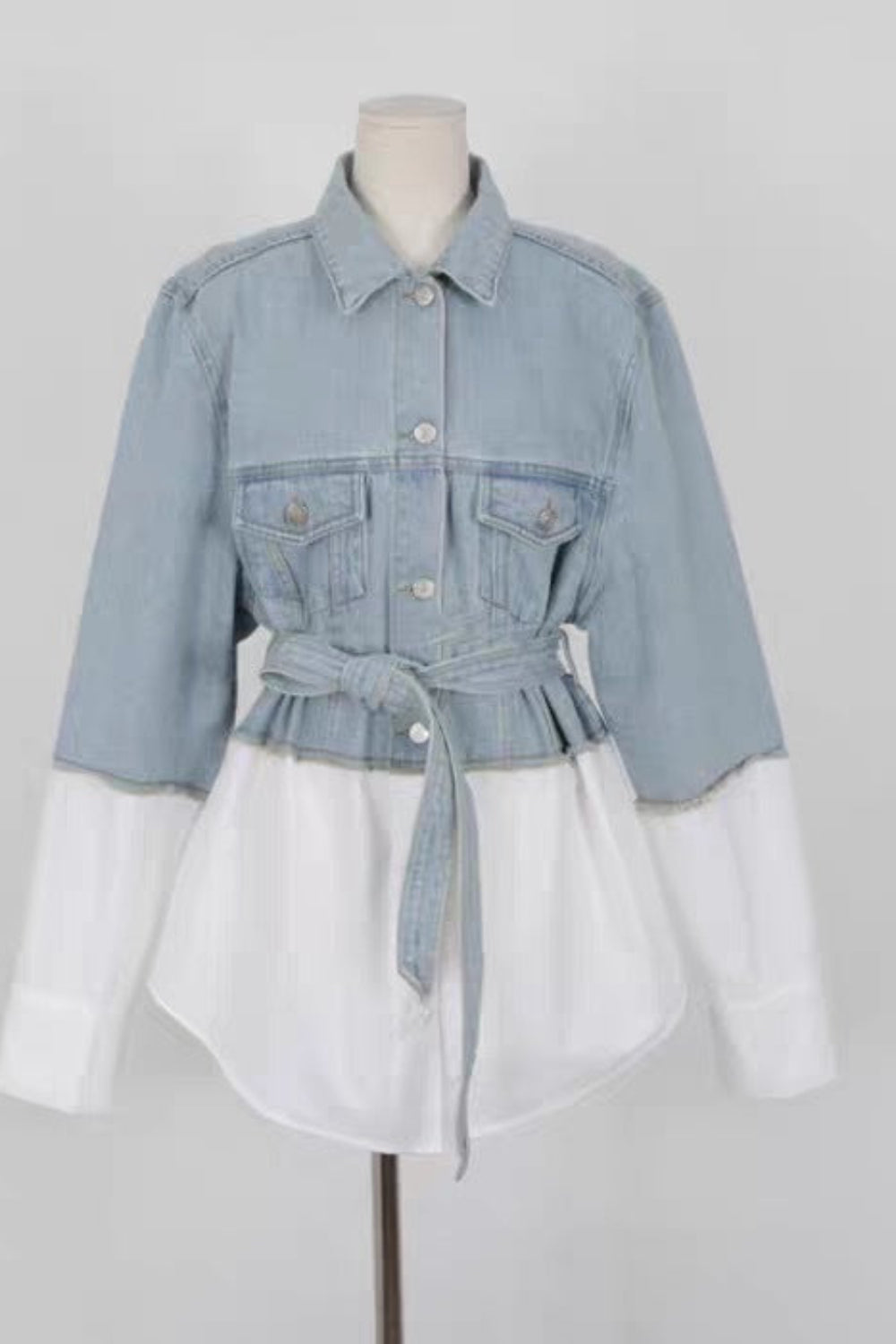 Denim jacket with a white dress underneath on a mannequin against a gray background
