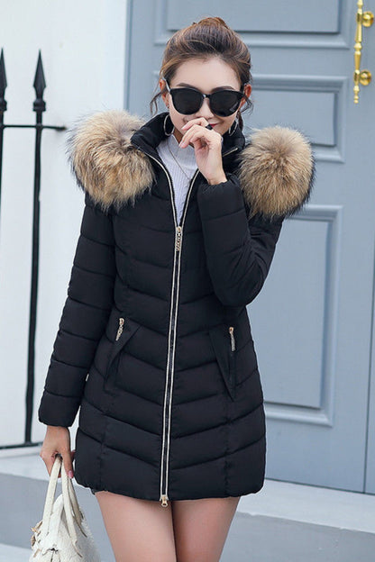 Woman wearing a black puffer coat with fur hood in front of a gray door.