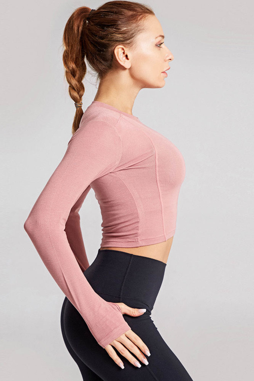 Woman wearing a pink long-sleeve crop top and black leggings on a light gray background