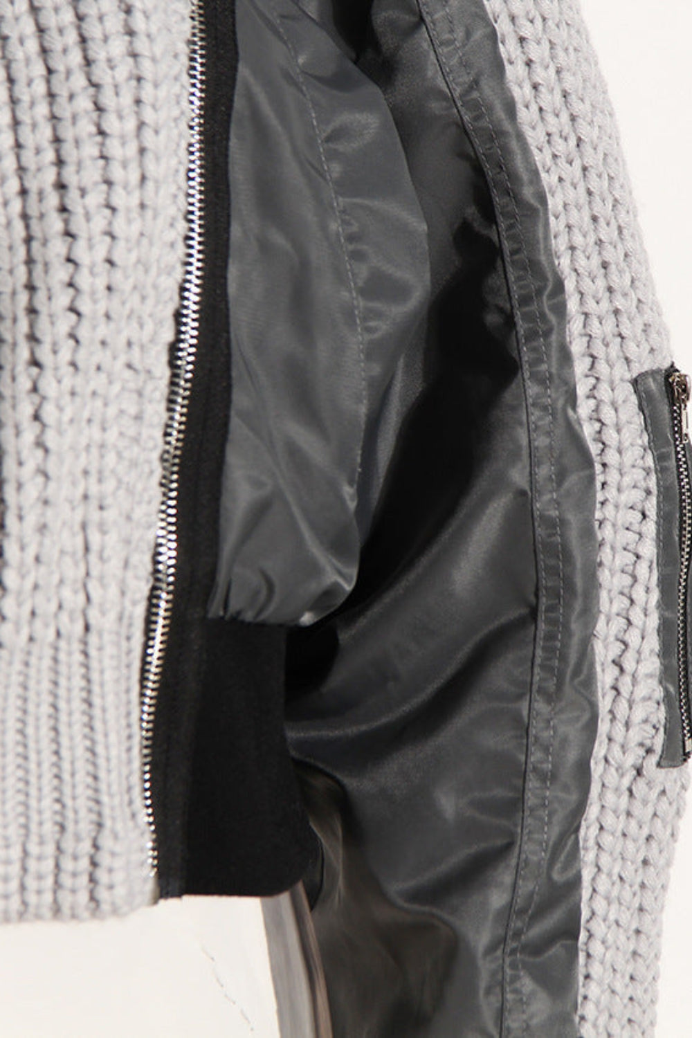 Close-up of a textured gray sweater with a zipper pocket on a white background