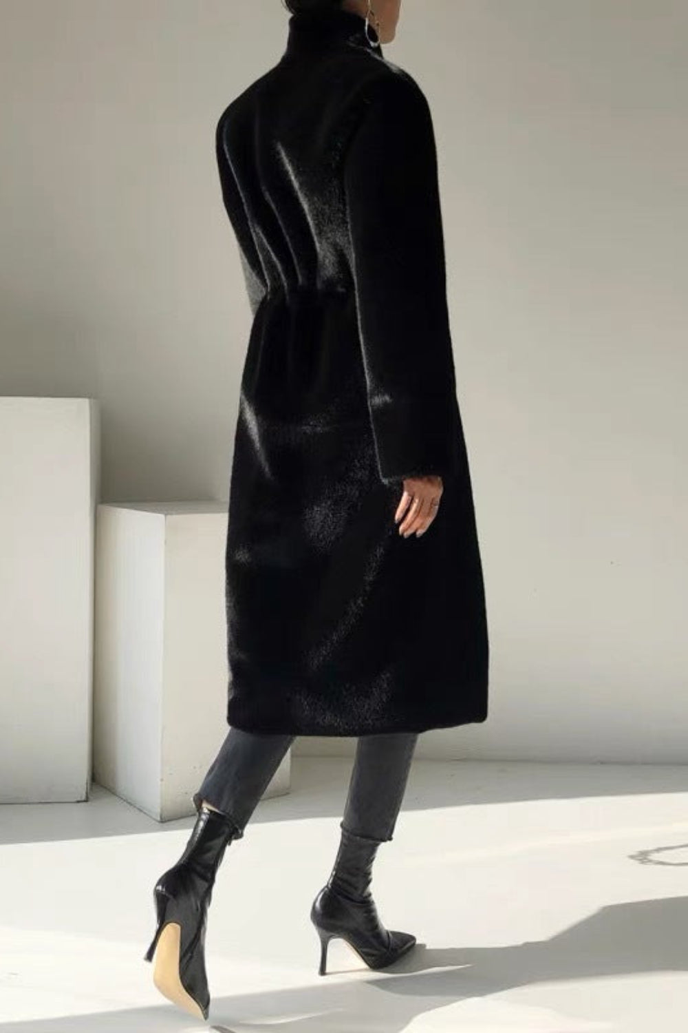 Person wearing a black coat in a minimalistic setting