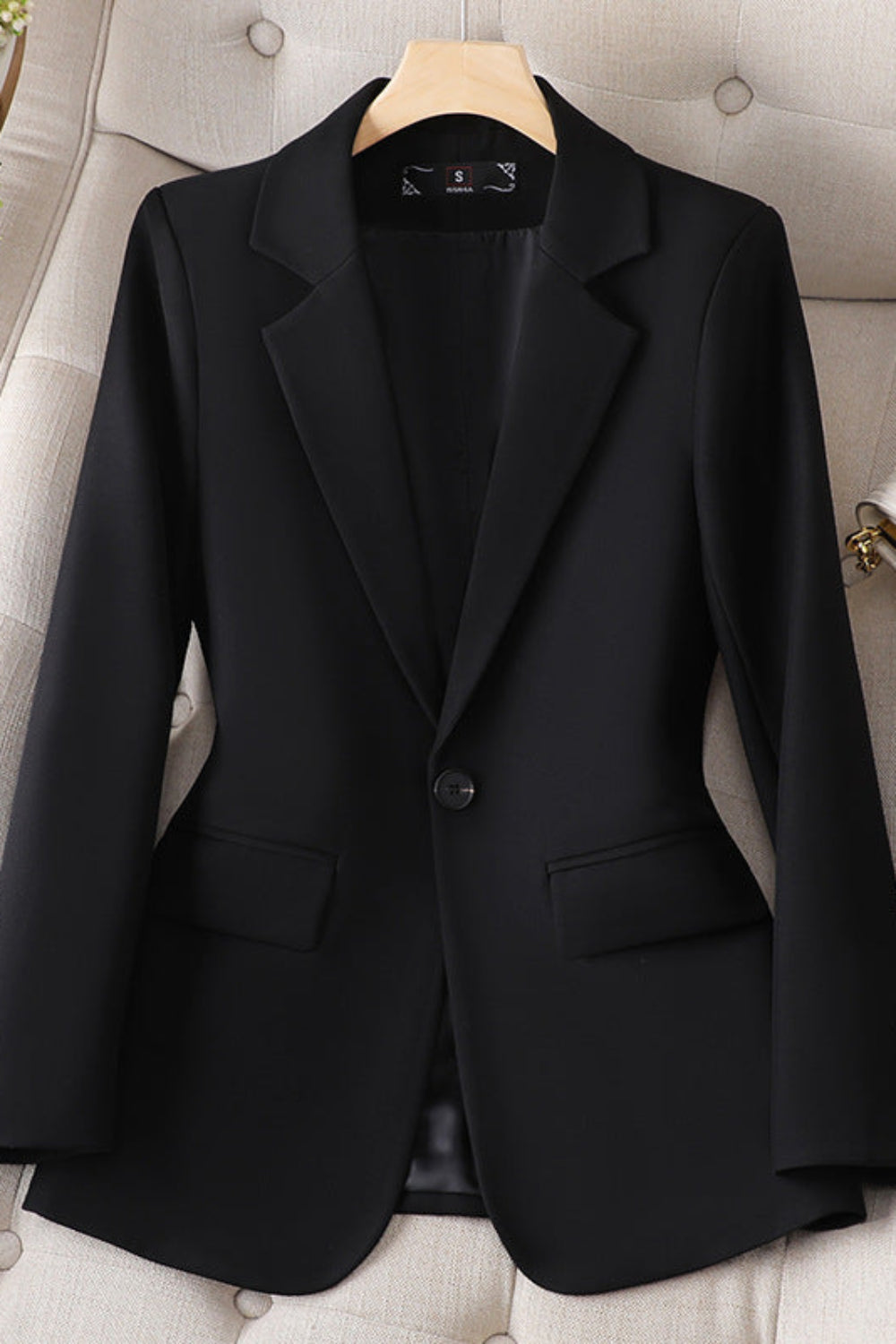 Black blazer on a hanger against a neutral background