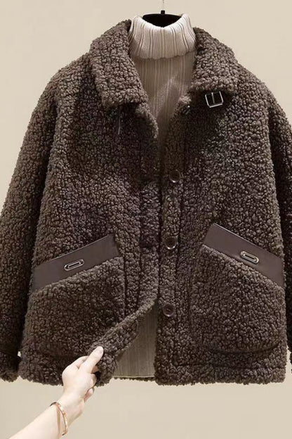 Brown sherpa jacket with a hand holding it against a beige background