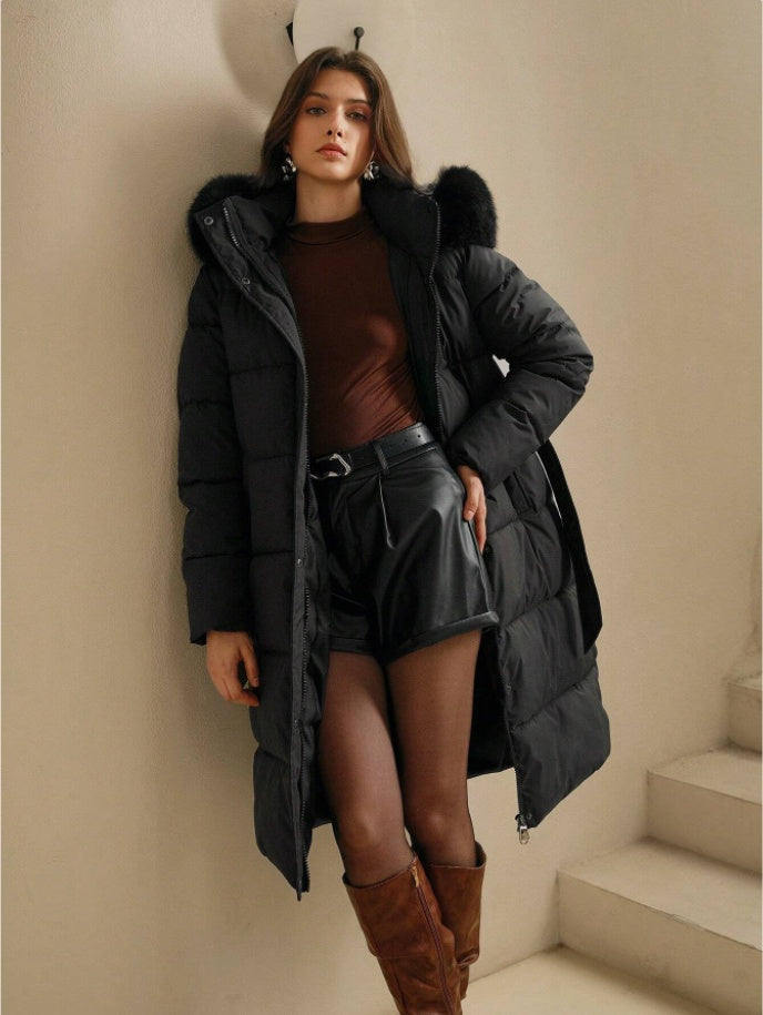 Woman wearing a long black puffer coat with fur hood in an indoor setting.