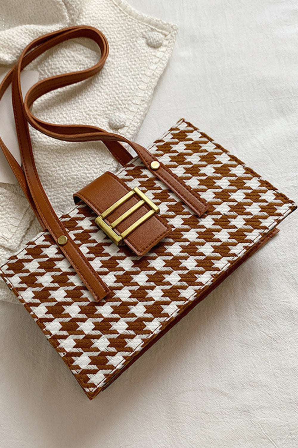 Patterned handbag with brown strap on a light fabric background
