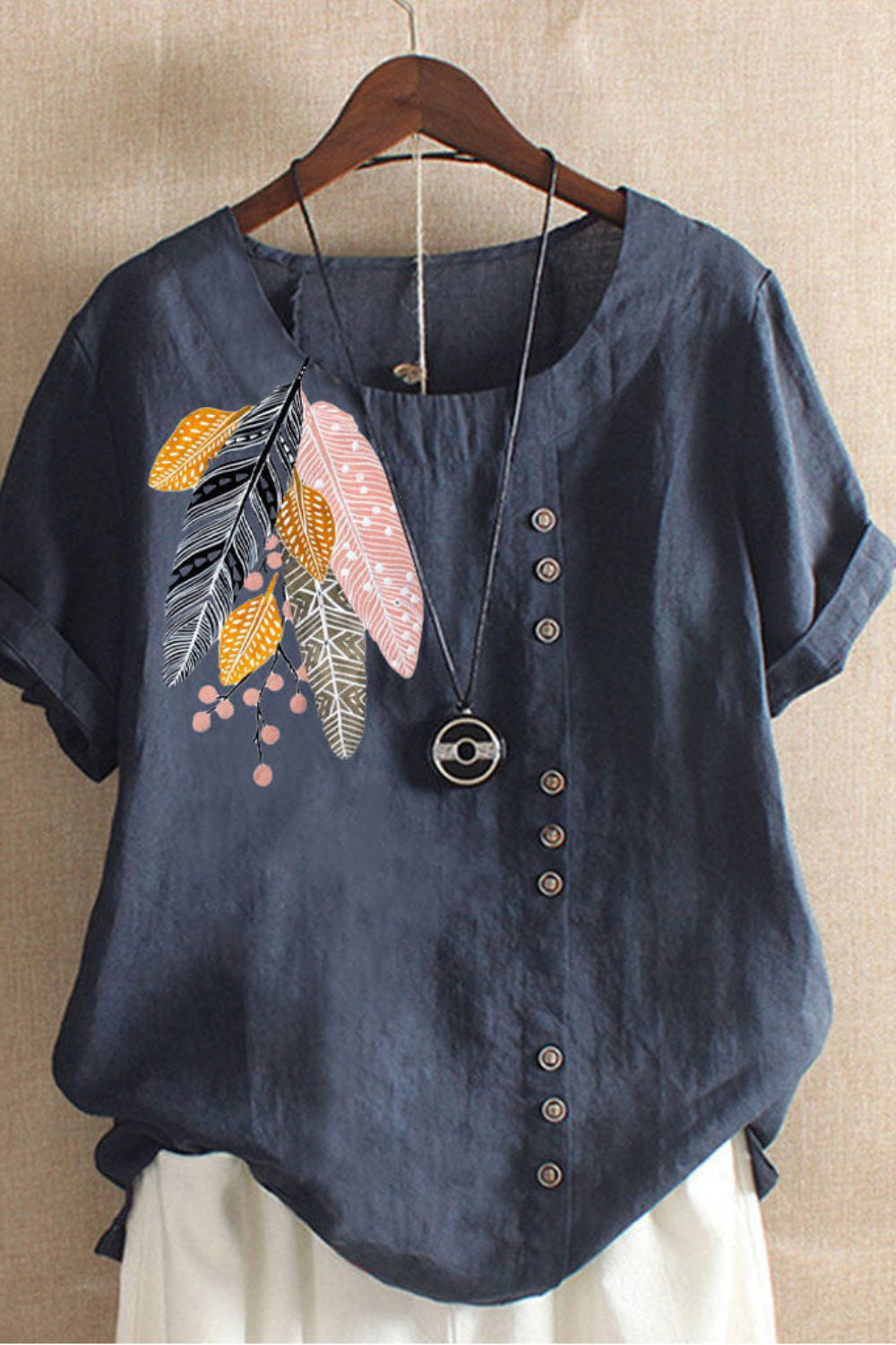 Blue shirt with floral embroidery on a hanger against a beige wall