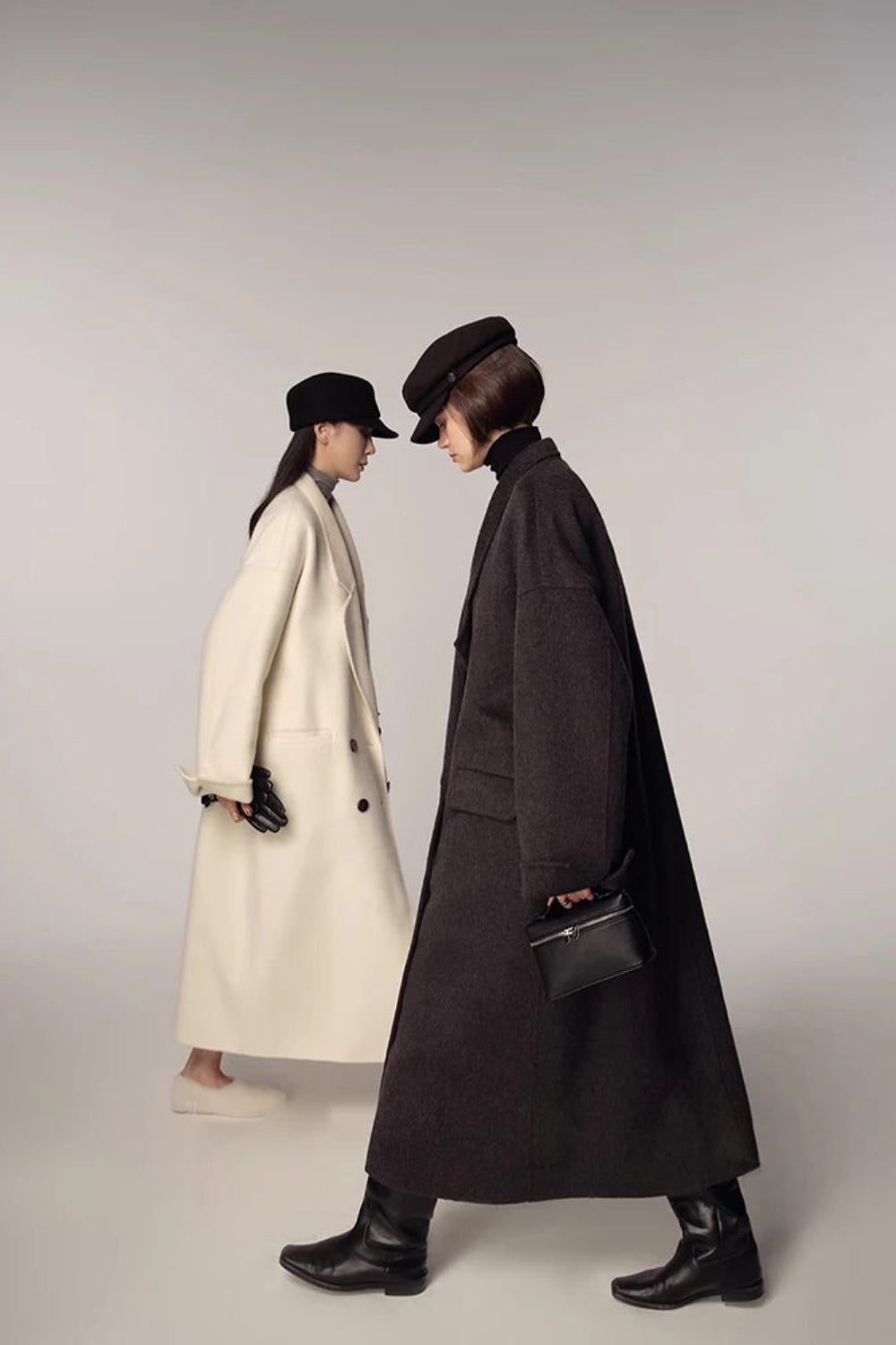 Two people wearing long coats and hats on a plain background