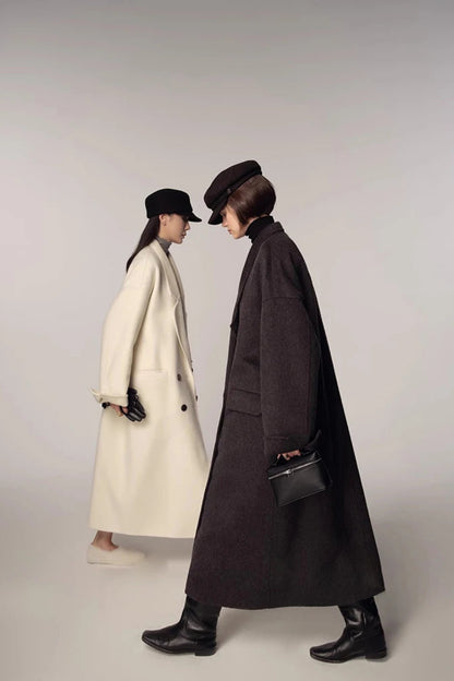 Two people wearing long coats and hats on a plain background
