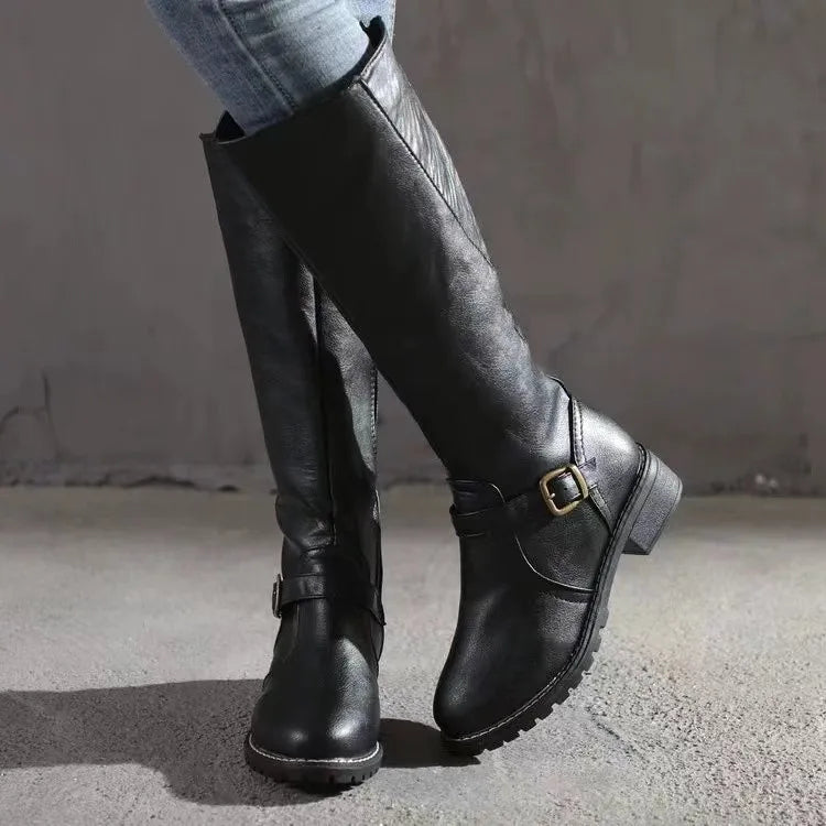 Black knee-high boots with a buckle on a neutral background
