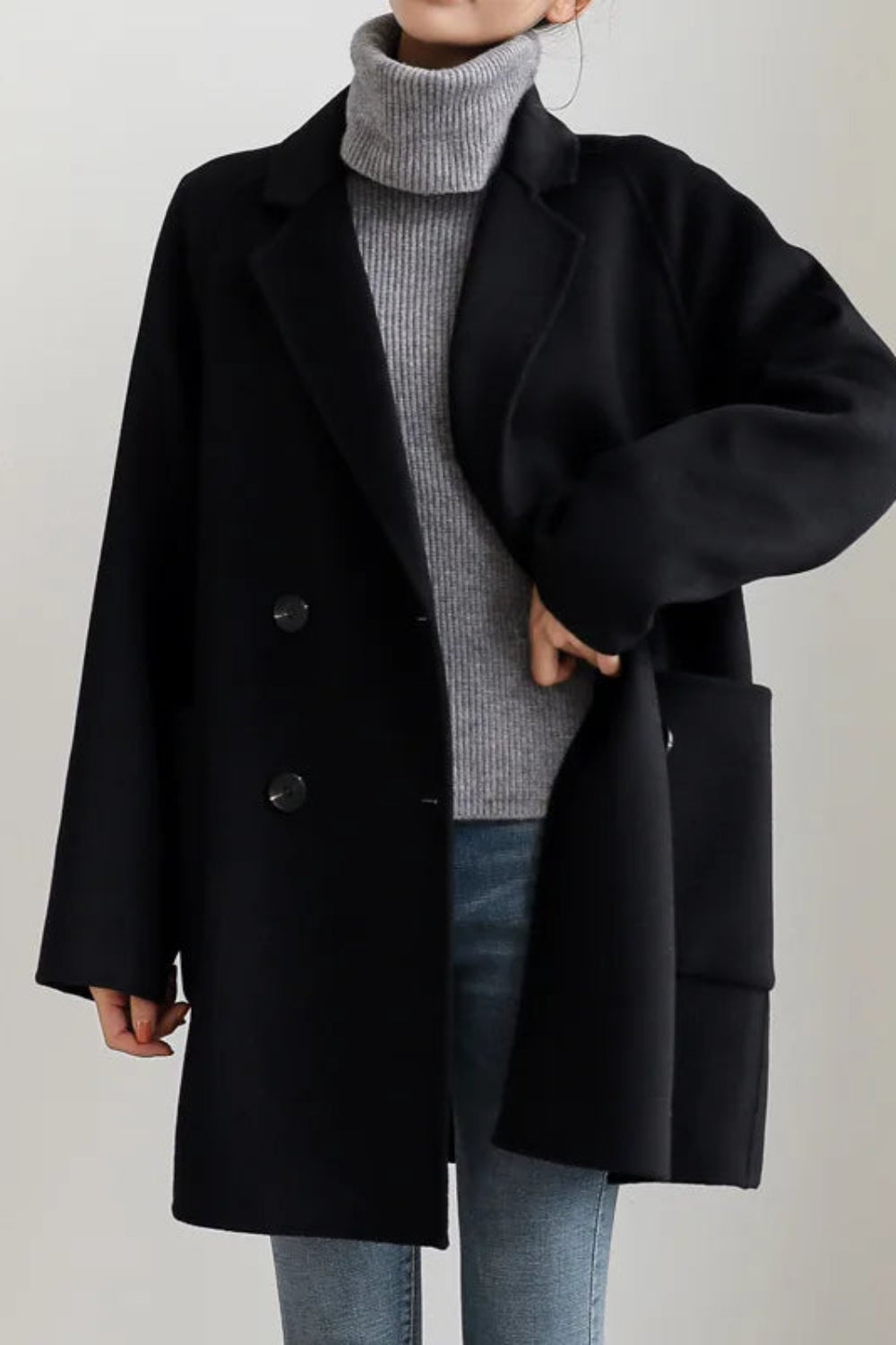 Person wearing a black coat over a gray sweater on a plain background