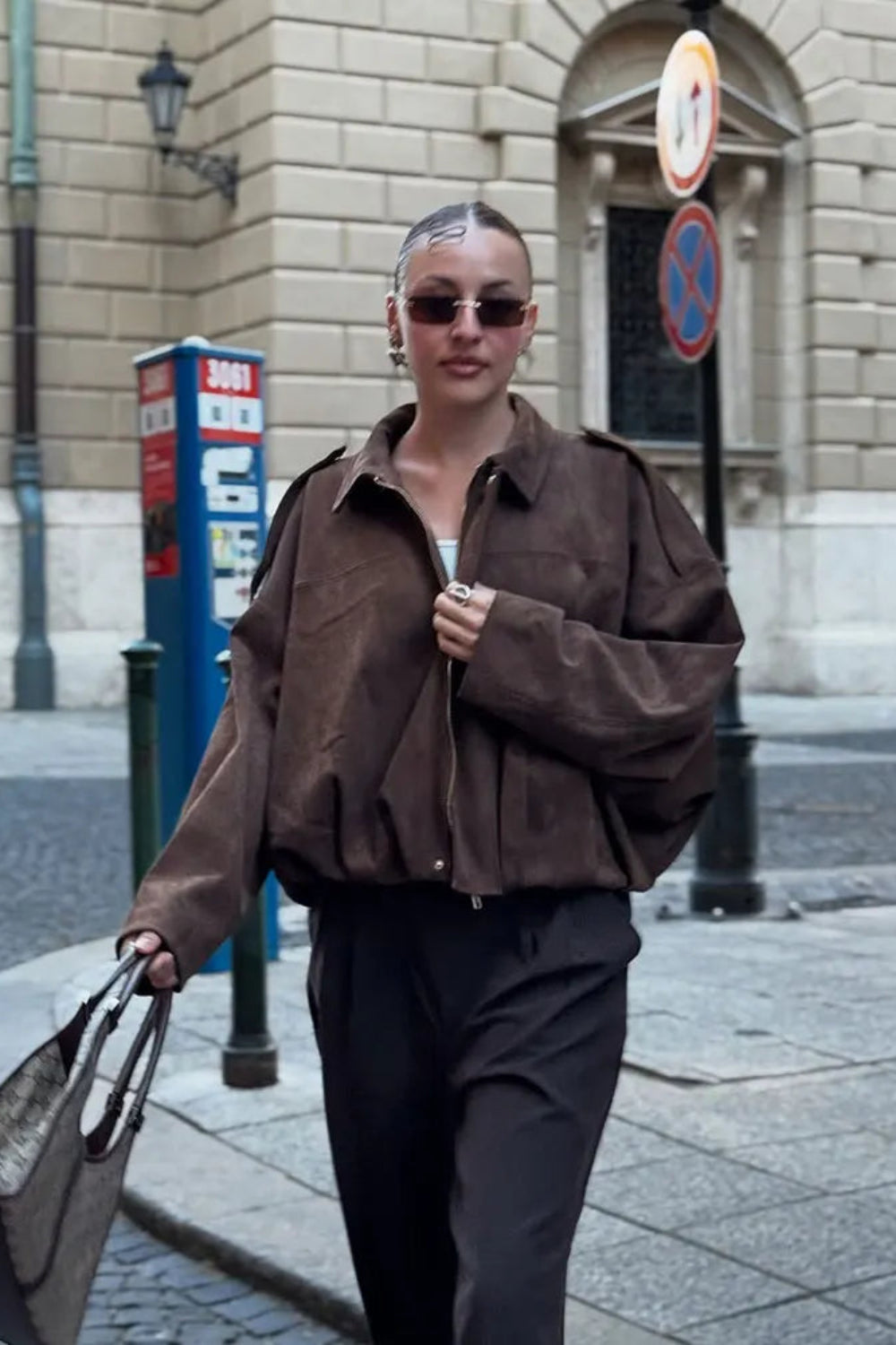 Person wearing a brown jacket and sunglasses on a city street.