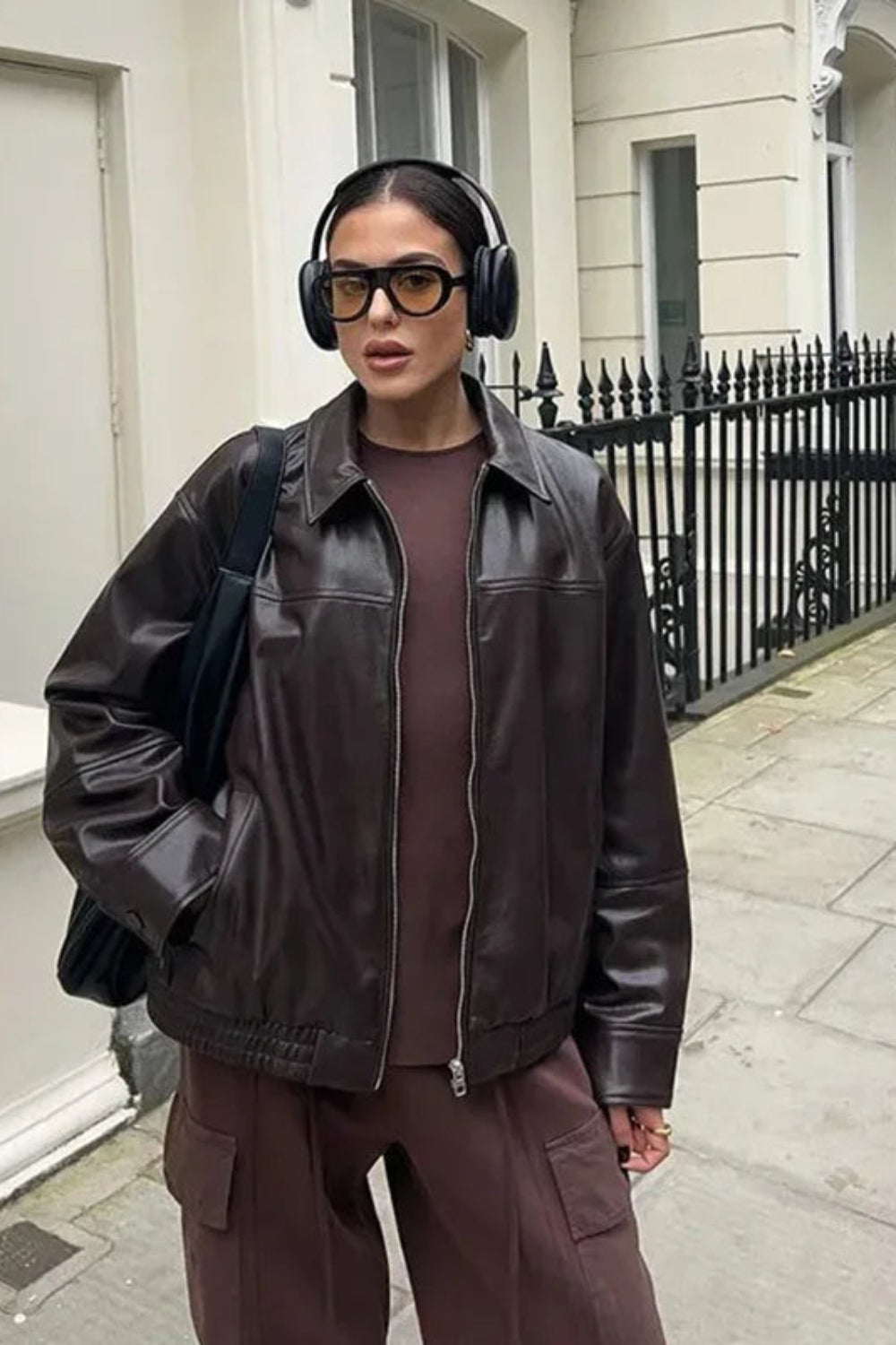 Person wearing a brown leather jacket and pants with headphones in an urban setting.