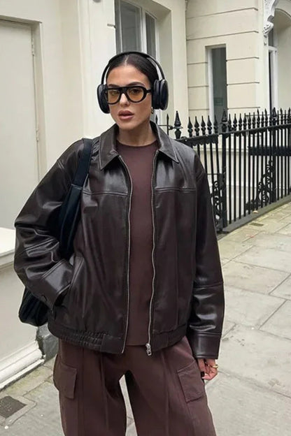 Person wearing a brown leather jacket and pants with headphones in an urban setting.