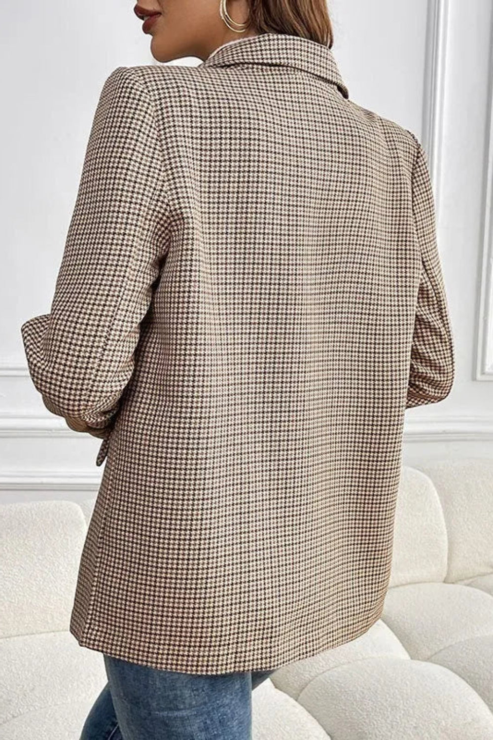 Person wearing a plaid blazer in a minimalistic room with white walls and furniture.