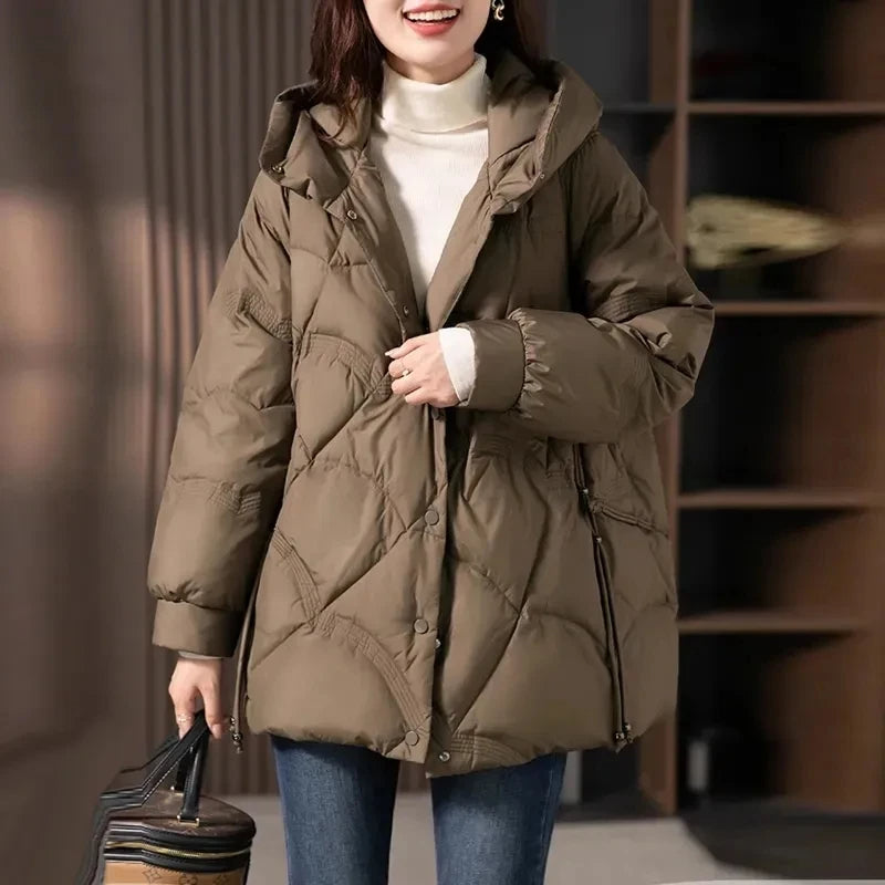 Person wearing a brown puffer jacket holding a suitcase indoors.