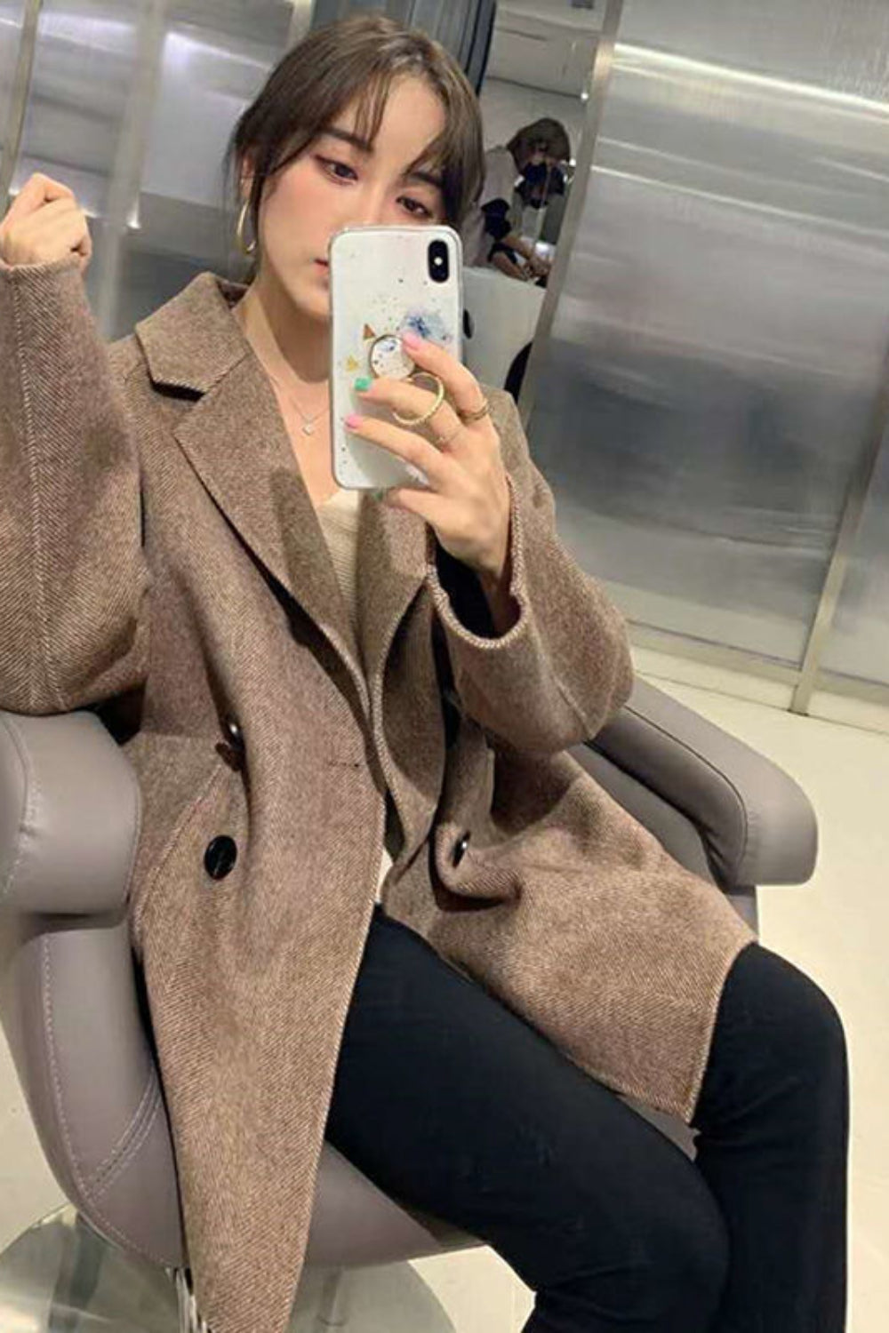 Person wearing a brown coat sitting on a chair indoors.