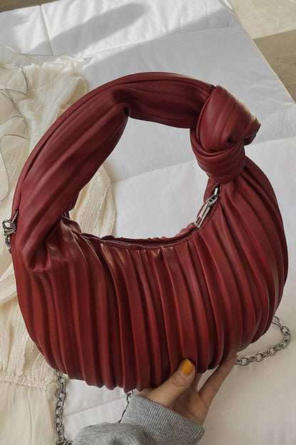 Red pleated handbag held by a hand on a light fabric background