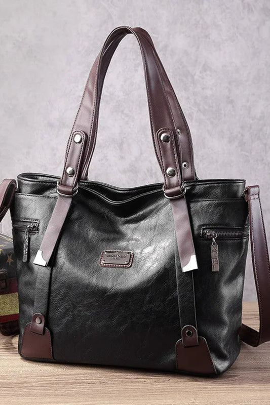 Black handbag with brown straps on a wooden surface with a gray textured background
