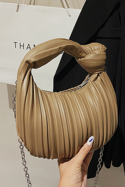 Beige pleated handbag with chain detail held by a person, with a blurred background