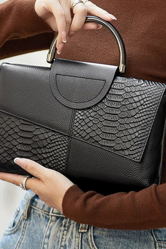 Person holding a black handbag with snake skin pattern