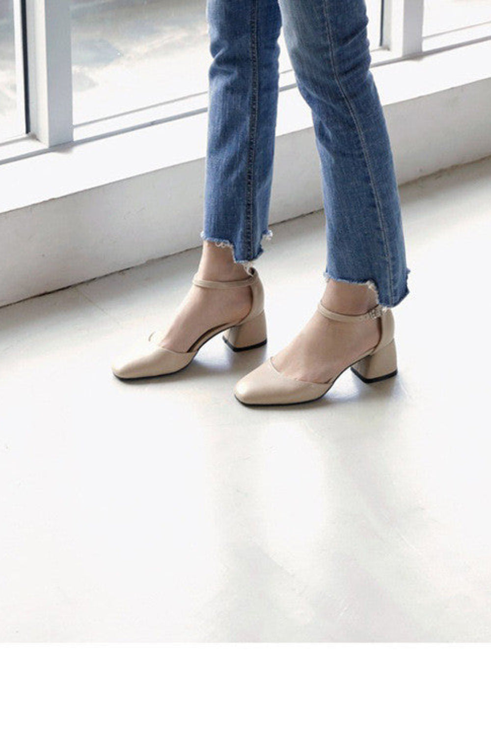 Beige high-heeled shoes worn with blue jeans on a light wooden floor.