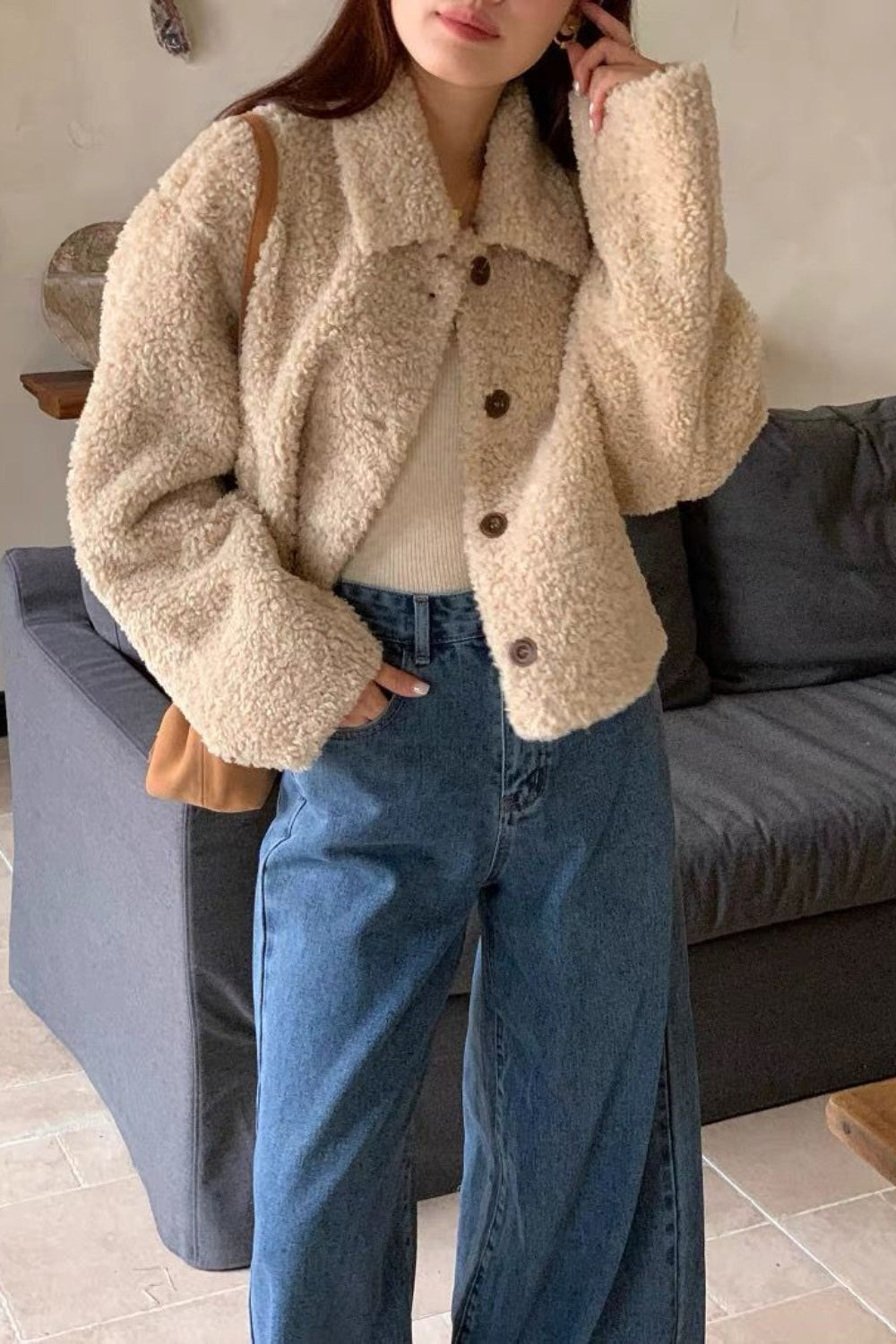 Person wearing a beige sherpa jacket and blue jeans indoors.