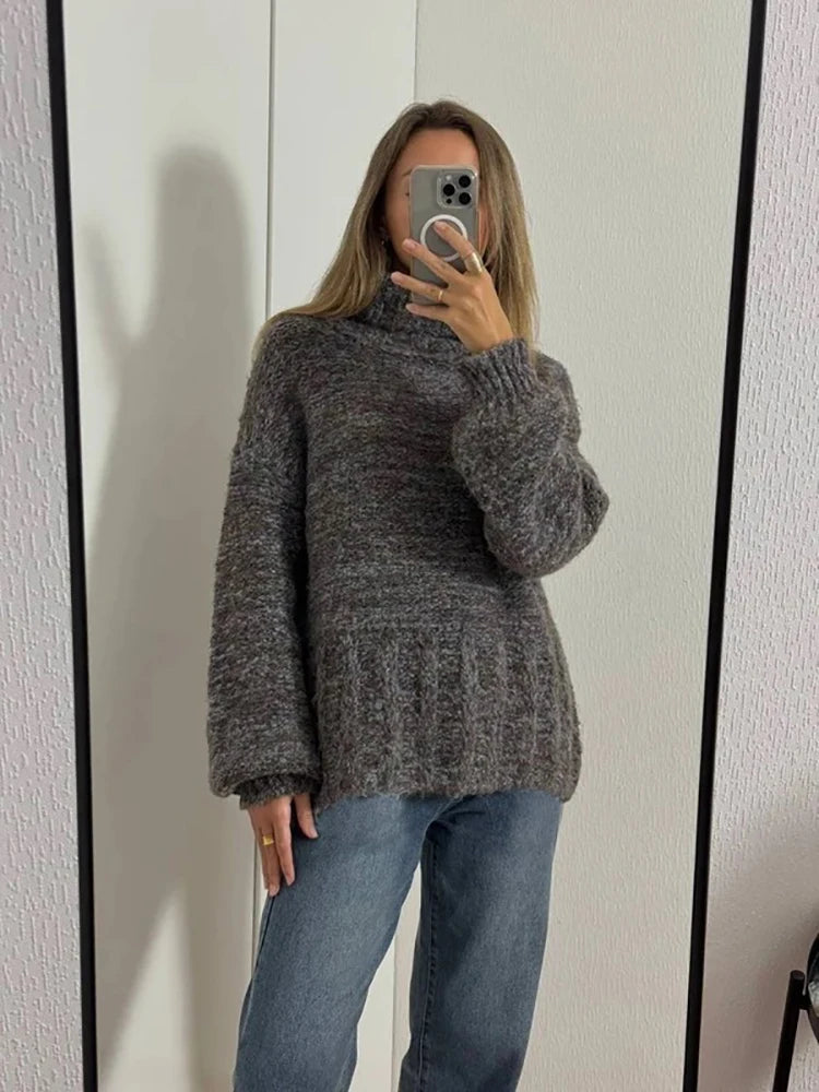 Person wearing a gray sweater and blue jeans taking a mirror selfie.