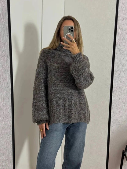 Person wearing a gray sweater and blue jeans taking a mirror selfie.
