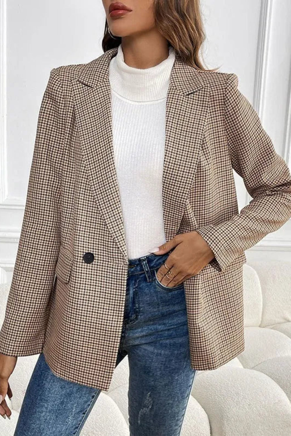 Person wearing a plaid blazer, white turtleneck, and blue jeans in a neutral setting